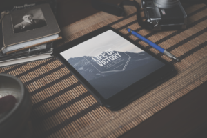 Tablet displaying a digital book cover titled ‘Life of Victory’ by Barry Tallis, placed on a bamboo mat beside a vintage camera, pencil, and old photo albums, symbolizing reflection, legacy, and spiritual growth
