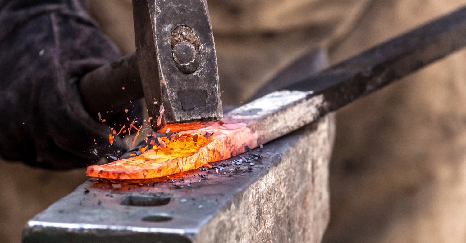 Close-up of a blacksmith hammering a glowing piece of hot metal on an anvil, with sparks flying, symbolizing craftsmanship, strength, and the forging process