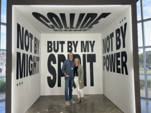 Barry & Dennette standing inside a modern photo booth at Collide Conference, surrounded by bold lettering that reads ‘Not by Might, Not by Power, But by My Spirit’ from Zechariah 4:6.