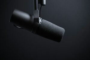 Close-up of a professional black podcast microphone on a boom arm against a dark background, symbolizing audio recording, broadcasting, and podcast production