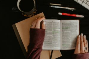 Woman studying the Bible at a desk with highlighted scripture, notebook, pens, and a cup of coffee, symbolizing personal devotion, faith, and quiet time with God