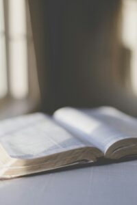 Open Bible resting on a table near a softly lit window, with natural light casting shadows, symbolizing peace, meditation, and quiet time with God’s Word